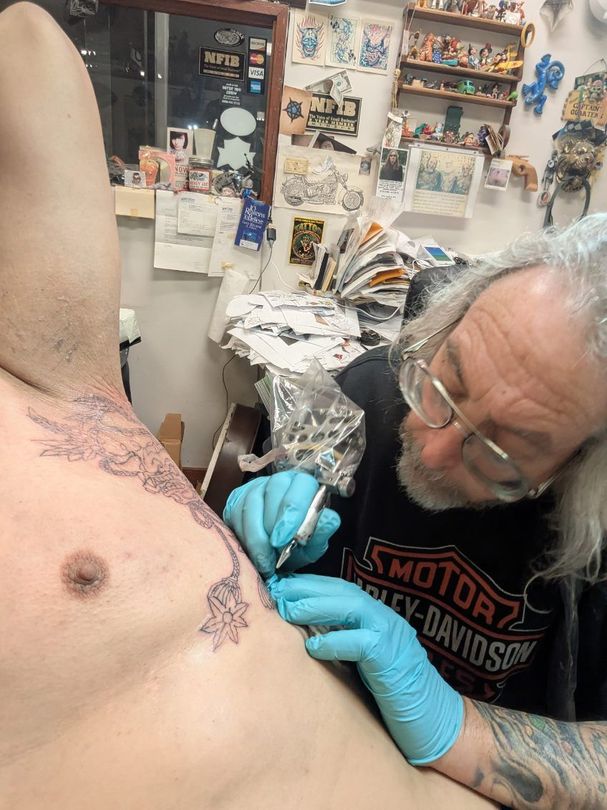 Tattoo artist working on a colorful back piece in a tattoo shop. Close-up of gloved hand and tattoo gun.