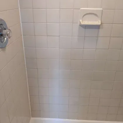 A shower stall with white tiles and a soap dish on the wall.