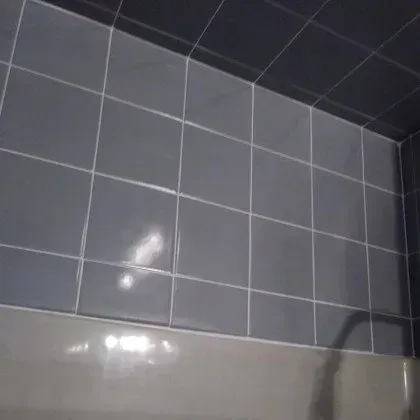 A bathroom with gray tiles on the wall and a bathtub.
