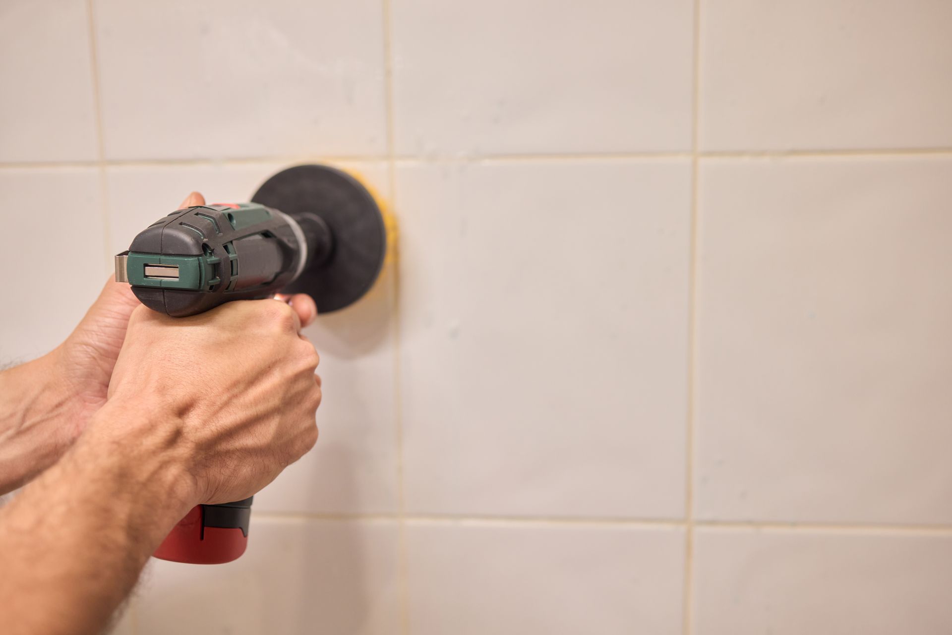 A person is using a drill to clean a tile wall.