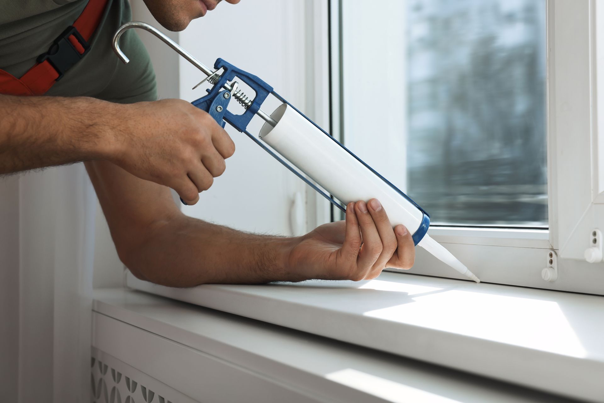 A man is applying caulk to a window sill.