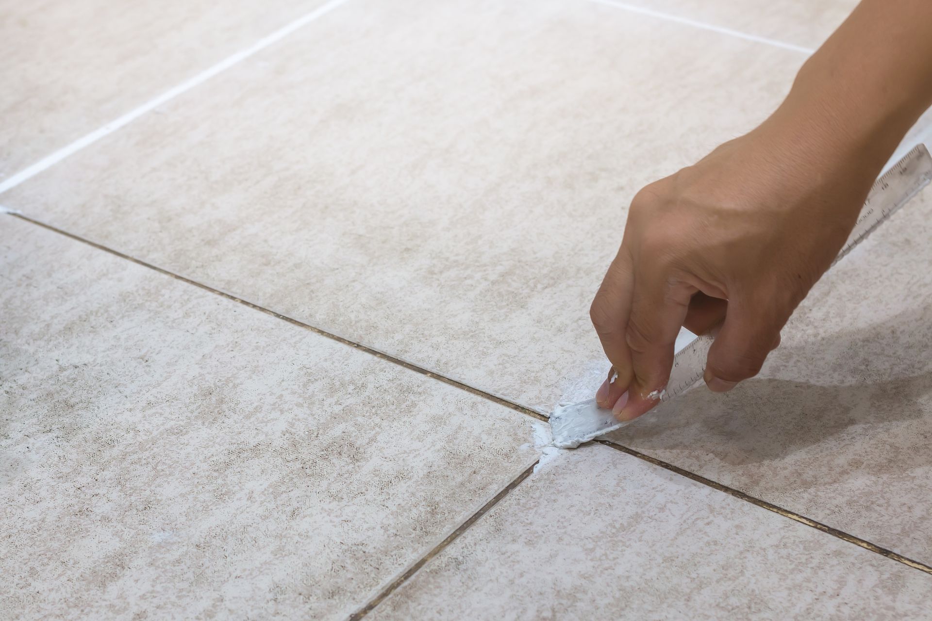 A person is applying a sealant to a tile floor.