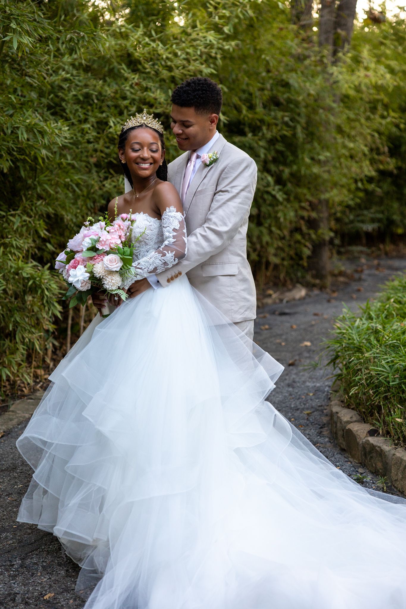 A bride and groom are standing next to each other on a path in the woods.