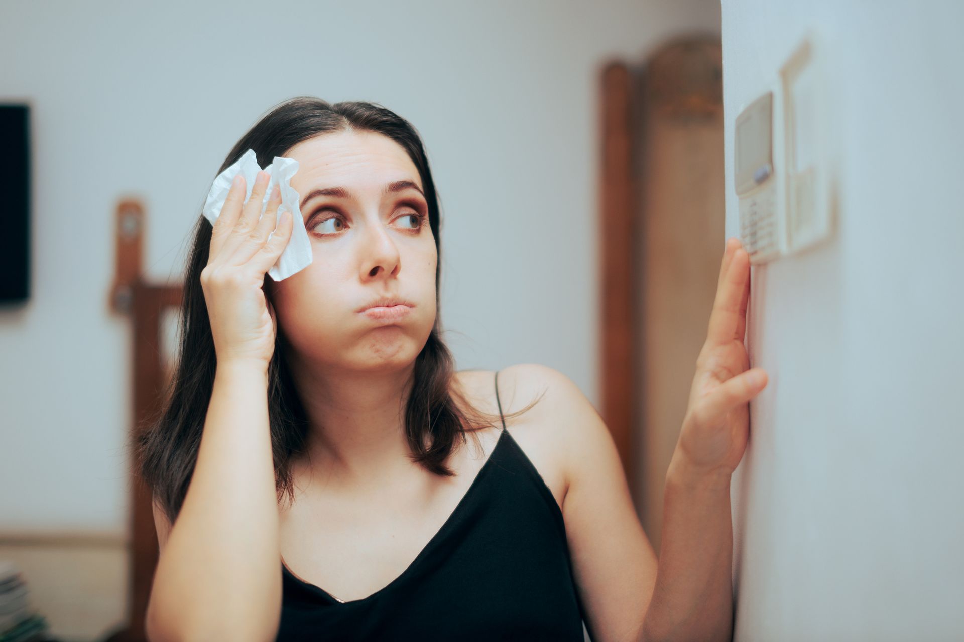 Woman feeling hot and needs AC repair next to the thermostat.