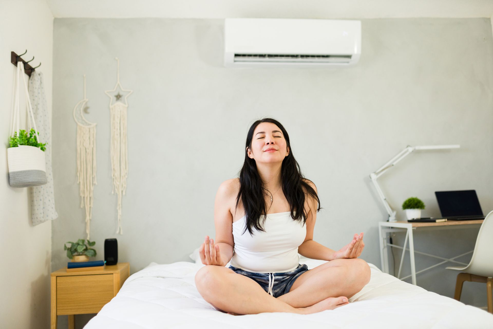 Woman meditates on a bed under a modern mini-split ac unit installed by Hoffner Heating & Air. 