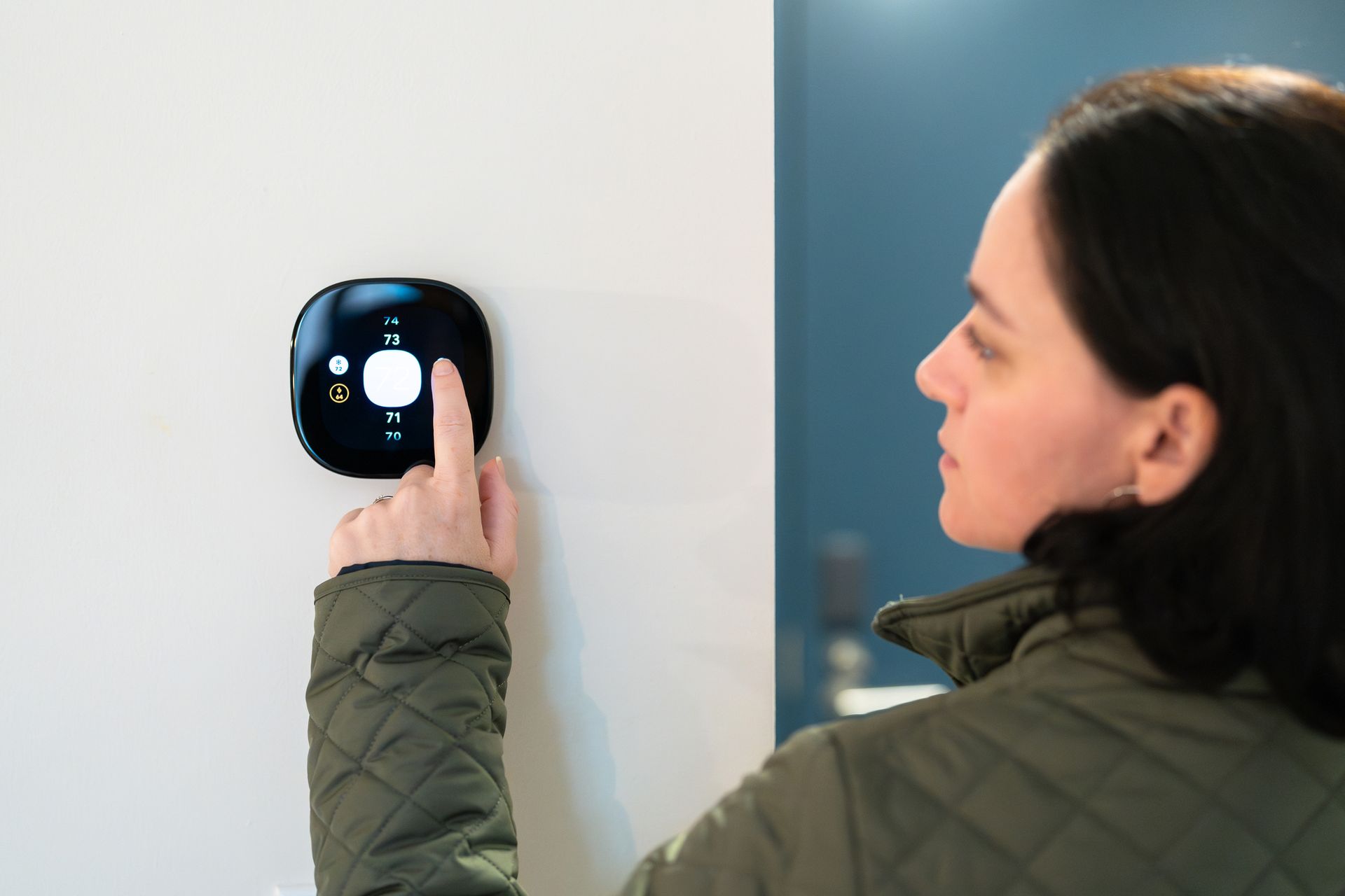 Woman adjusting temperature on digital thermostat.