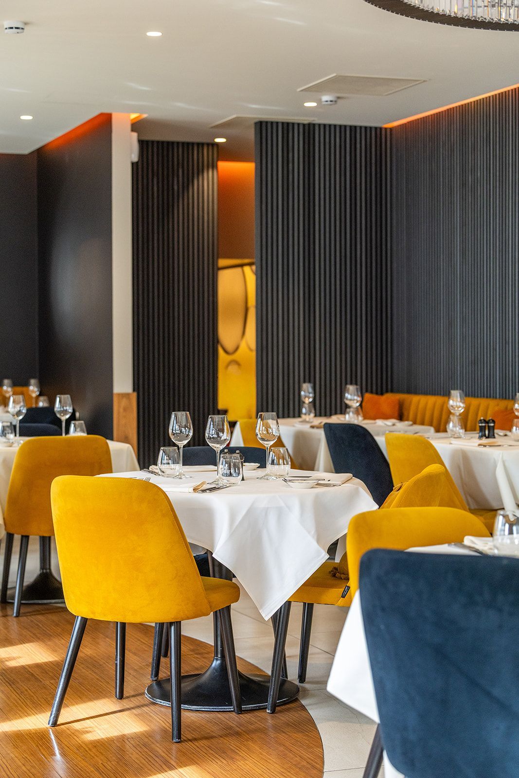 A table set for dining in a restaurant with exposed brick walls, a window overlooking a bar, and yellow and green chairs.