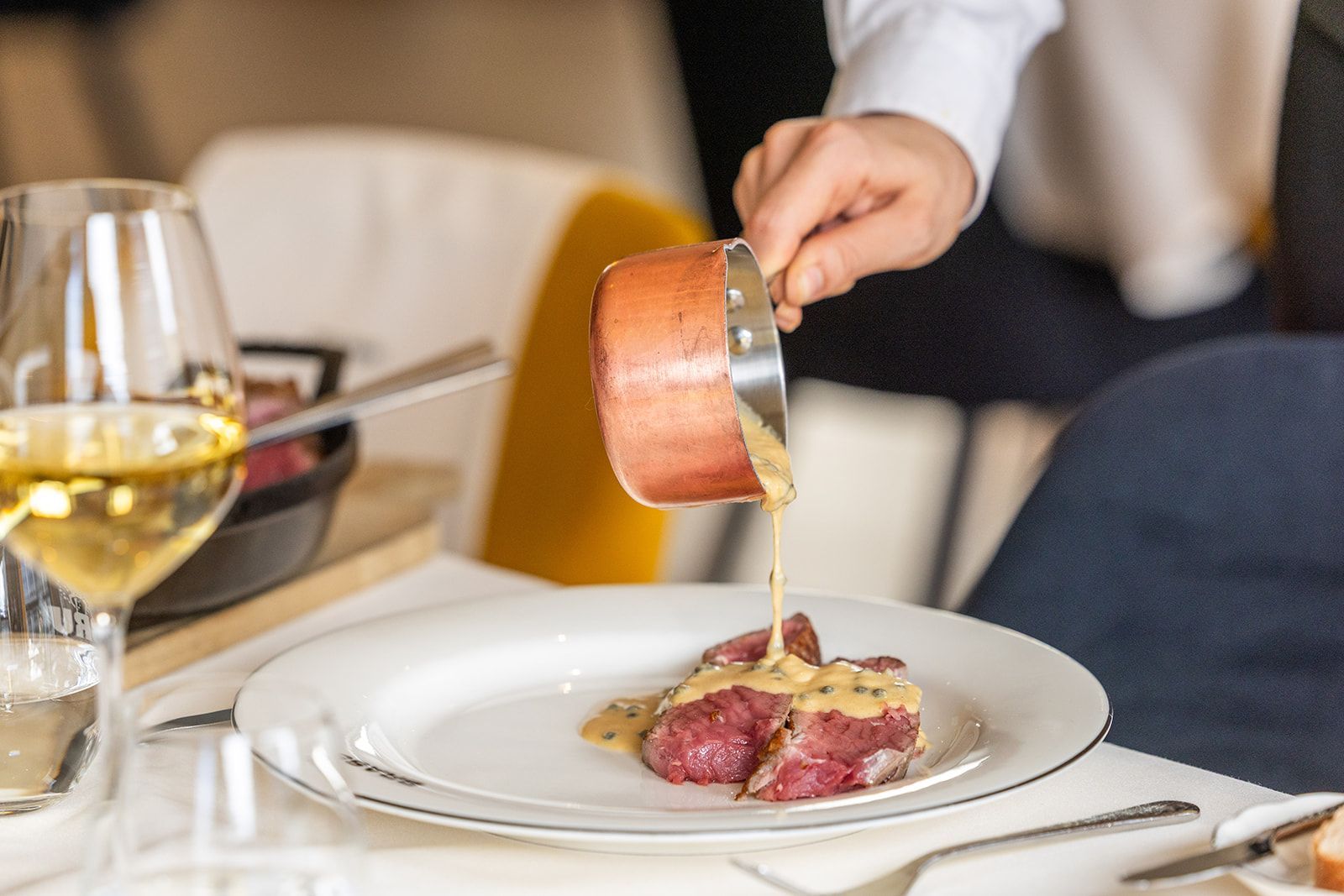 A white door frame looking into a room with a dark-wood fireplace, a dining table with yellow chairs, and tiled floors.