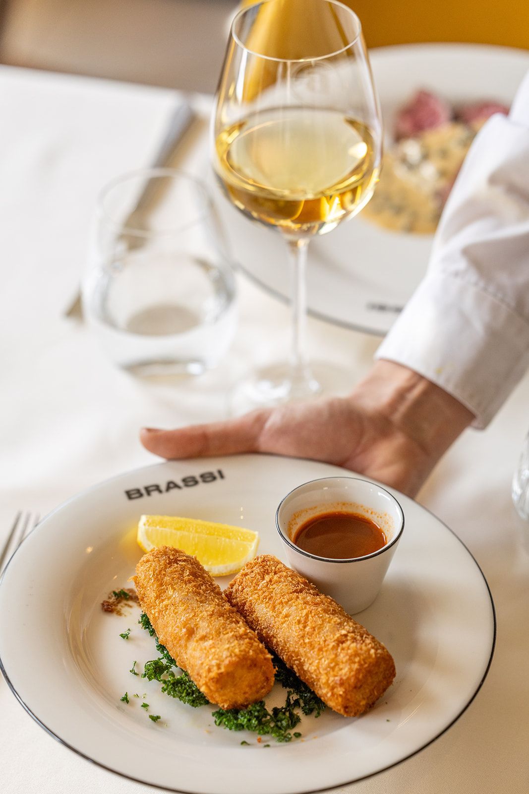 A restaurant interior with two tables, yellow and patterned chairs, brick flooring, and deer head wall decor.