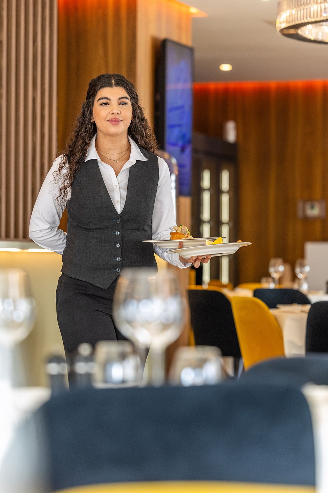 A close-up view of a chef’s hands using a metal spoon to arrange glazed, diced vegetables onto a wooden serving board.
