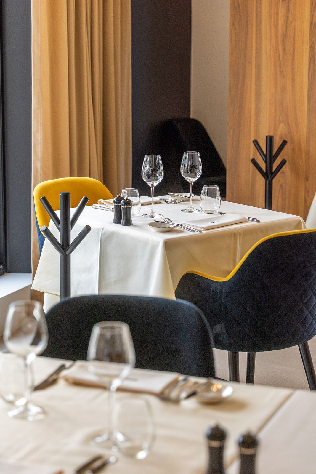 A smiling person stands in a restaurant wearing a patterned blouse and apron, holding two small plates of food.