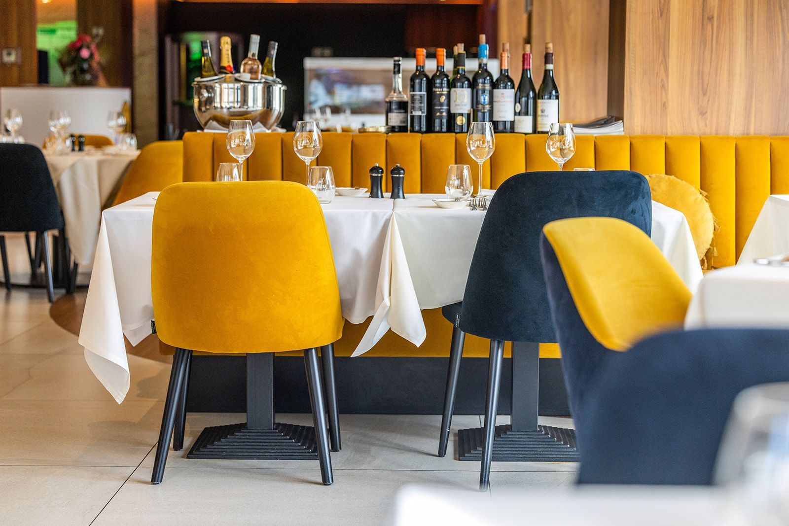 Two staff members in aprons smile and toast with glasses of white wine inside a restaurant.