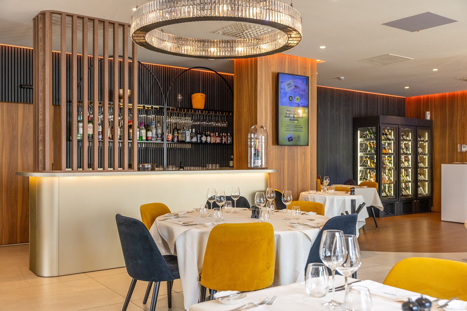 A bowl of green pesto pasta next to a wooden paddle with small appetizers on a leather placemat with glasses.