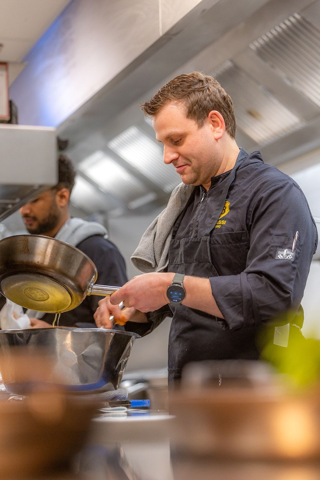 A restaurant interior featuring round tables with yellow chairs, a dark blue wall with a round gold light, and patterned tiles.