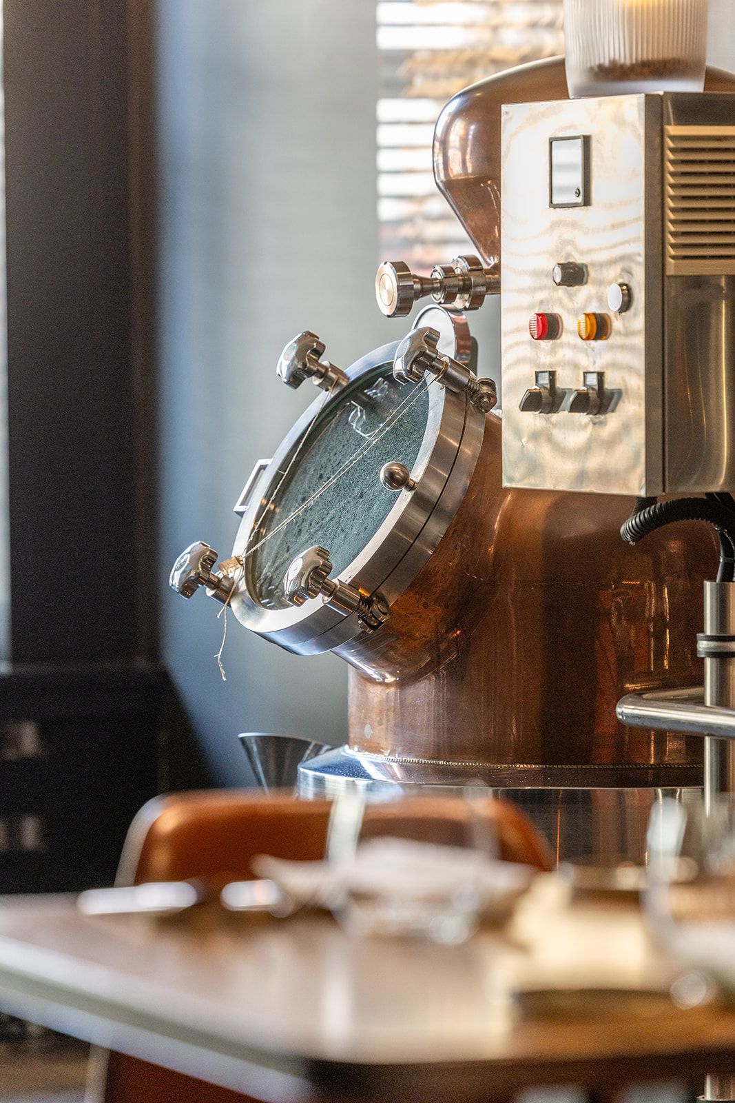Three smiling staff members in patterned blouses or a shirt and grey aprons stand together inside a brick-walled space.