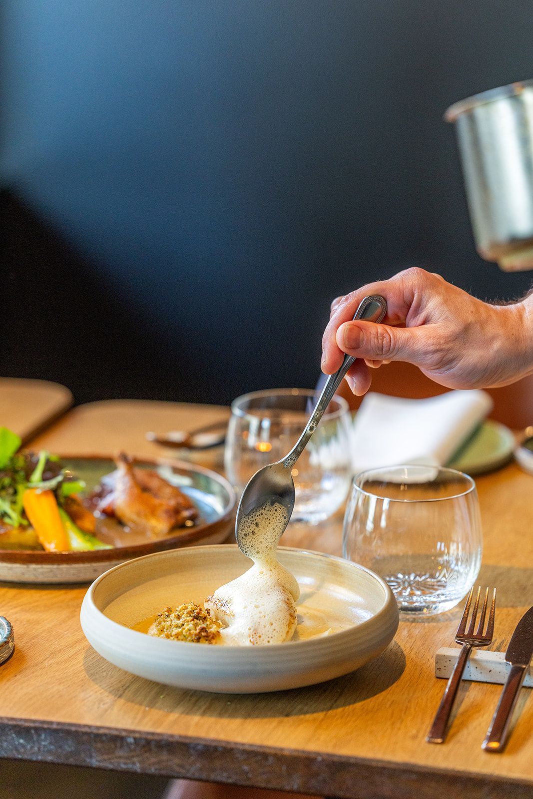 A close-up view of a chef’s hands using a metal spoon to arrange glazed, diced vegetables onto a wooden serving board.