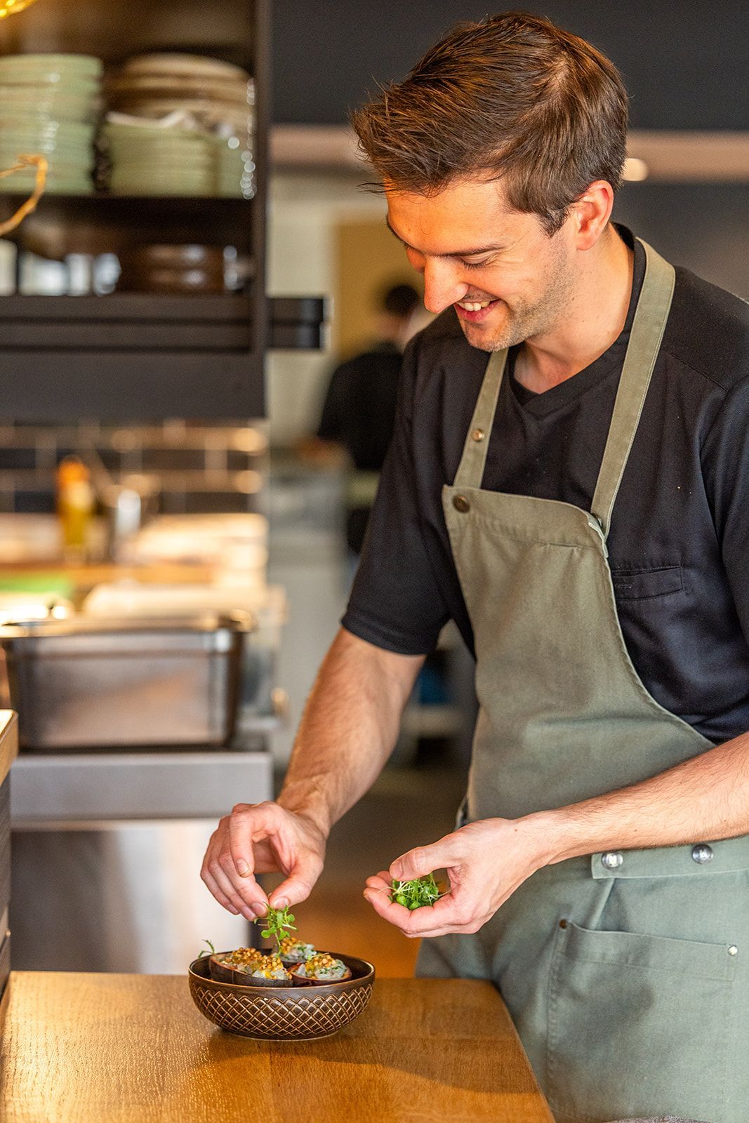 A restaurant interior featuring round tables with yellow chairs, a dark blue wall with a round gold light, and patterned tiles.