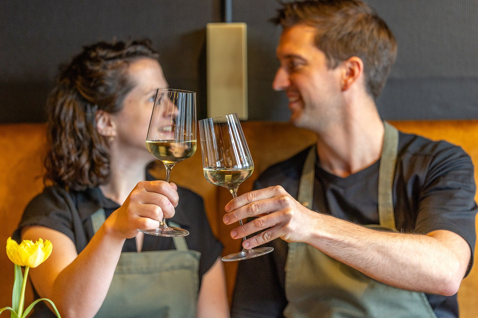 A restaurant interior with two tables, yellow and patterned chairs, brick flooring, and deer head wall decor.