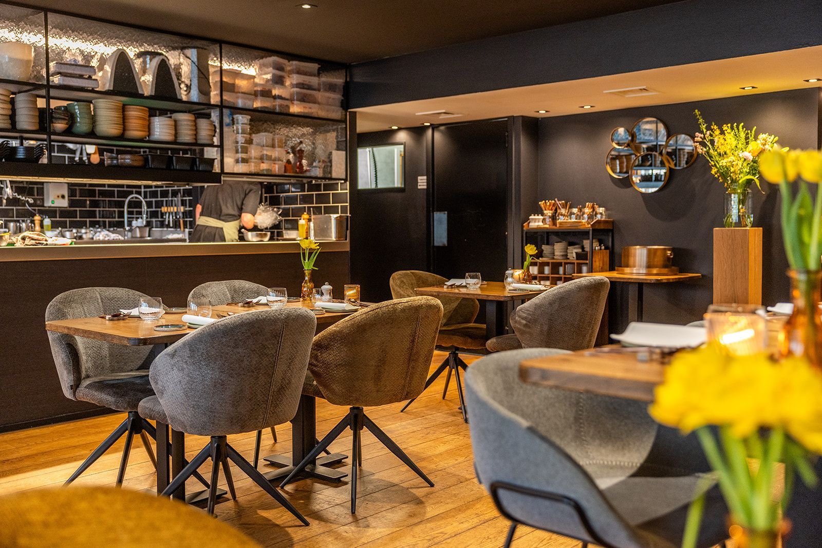 Two staff members in aprons smile and toast with glasses of white wine inside a restaurant.