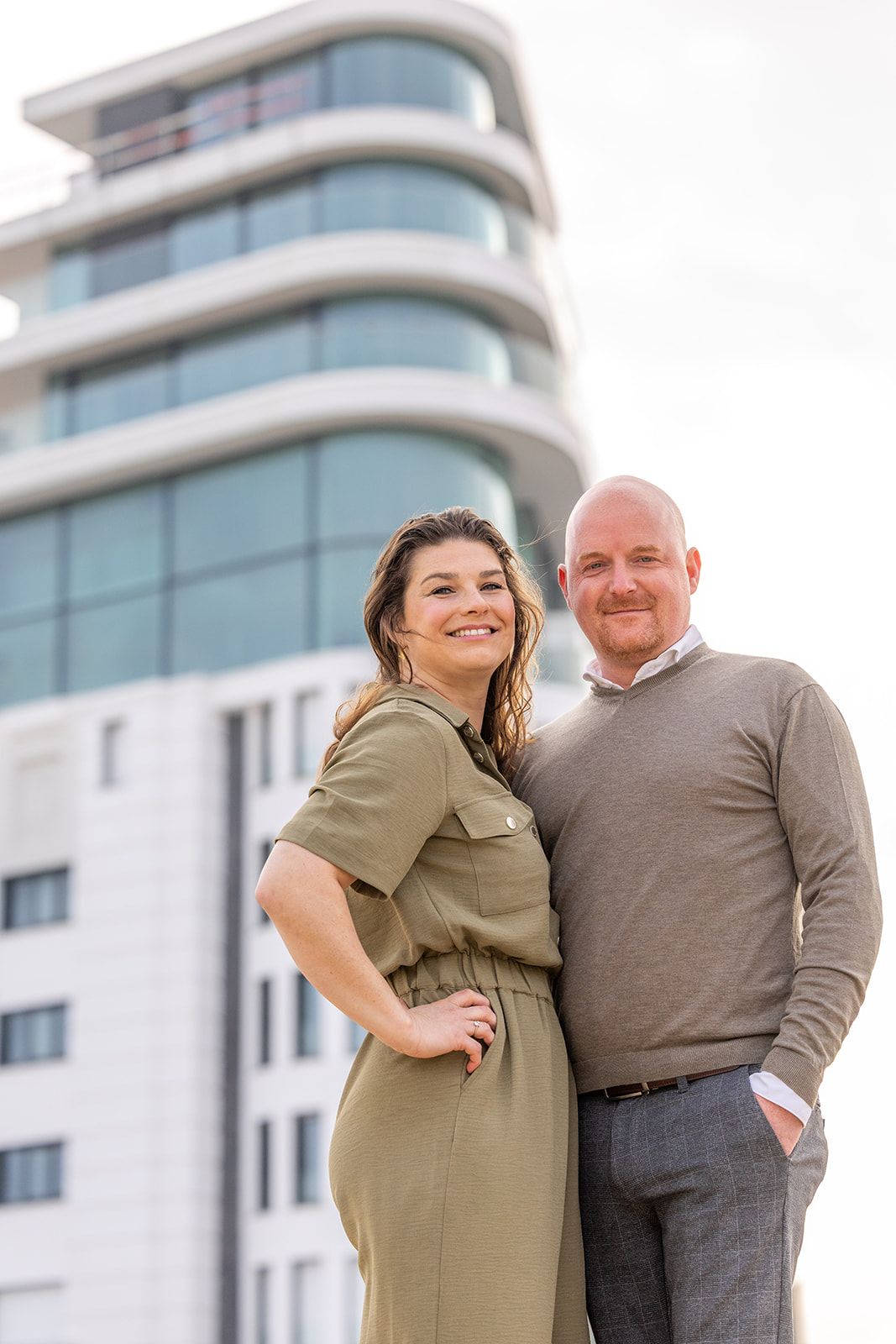 Two staff members in aprons smile and toast with glasses of white wine inside a restaurant.