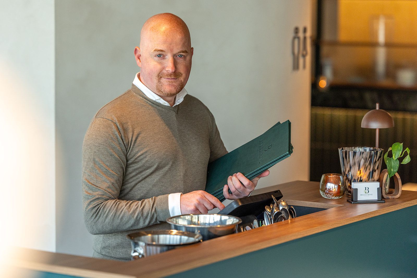 A restaurant interior with two tables, yellow and patterned chairs, brick flooring, and deer head wall decor.