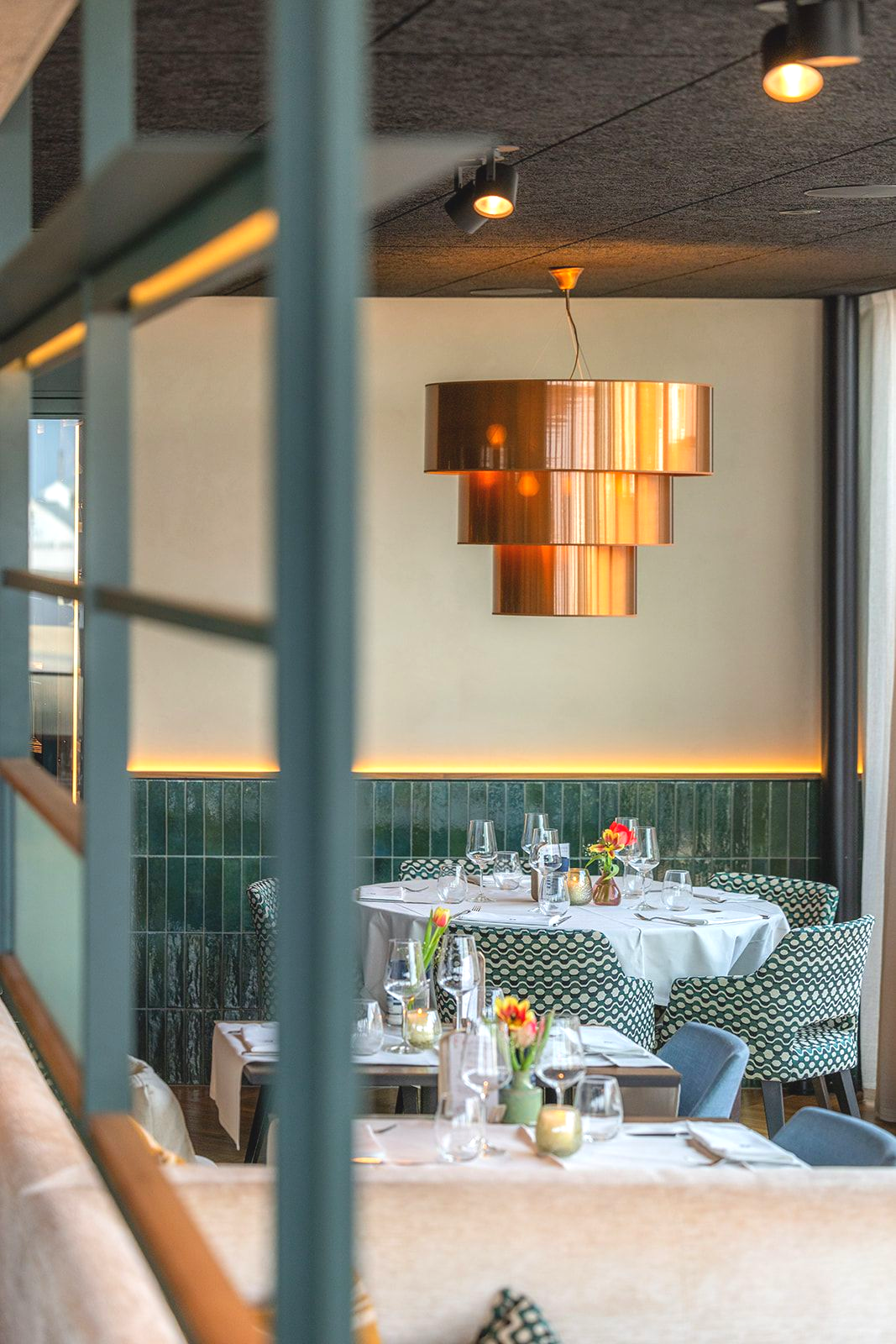 A bright, modern restaurant with wood floors, exposed brick, large windows, and yellow upholstered chairs at tables.