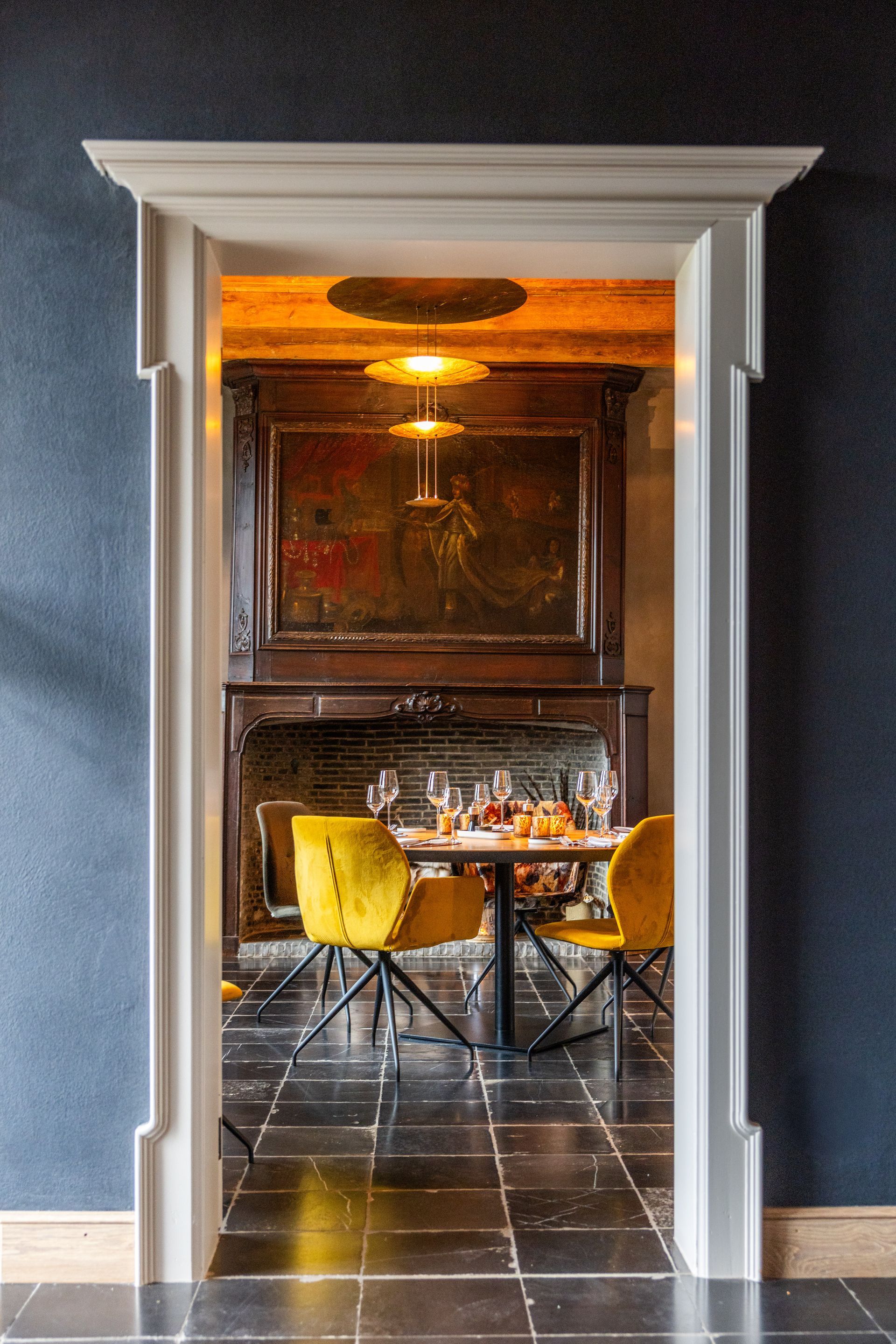 A white door frame looking into a room with a dark-wood fireplace, a dining table with yellow chairs, and tiled floors.