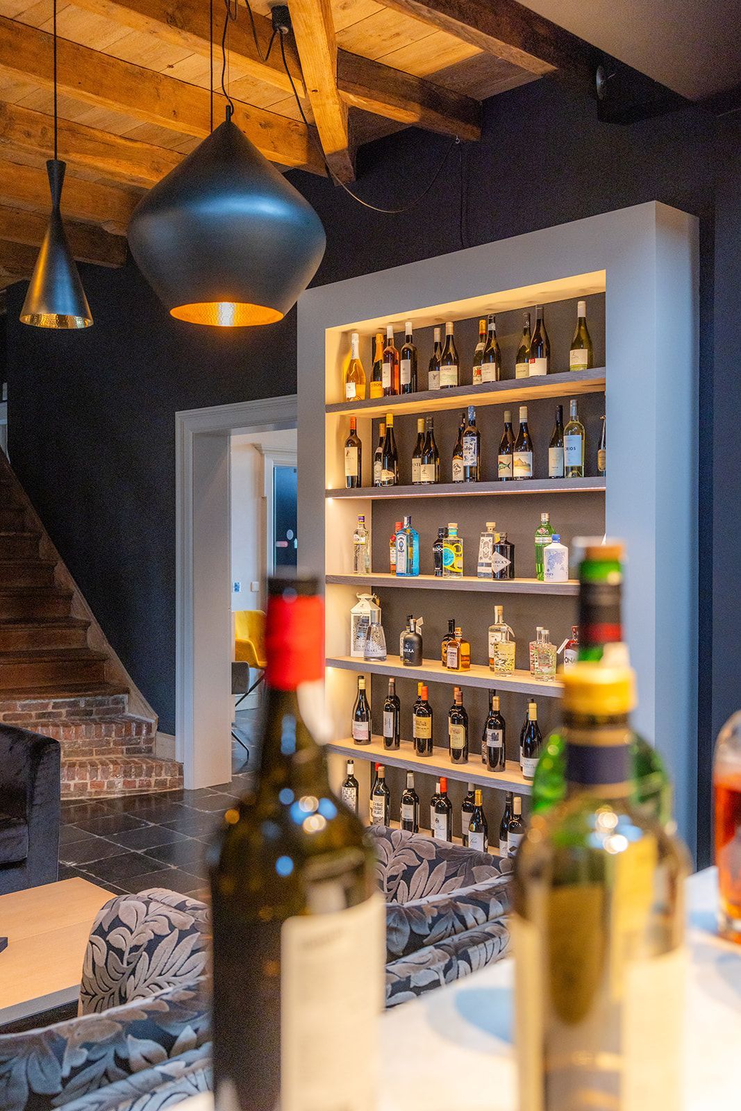 Interior view of a modern bar with a backlit shelf of various bottles and two bottles in the foreground.