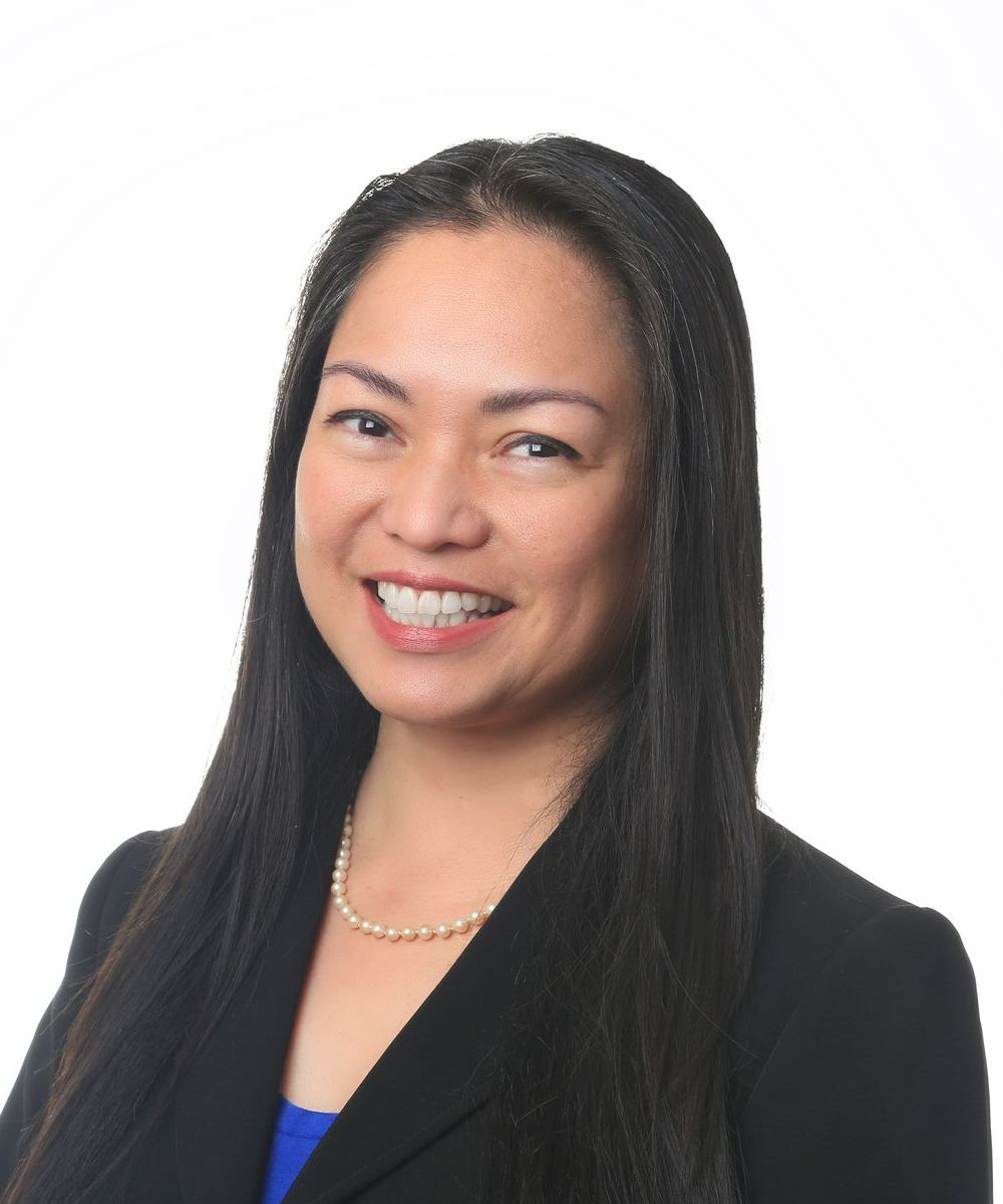 A woman is sitting at a desk with a laptop and a vase of flowers.