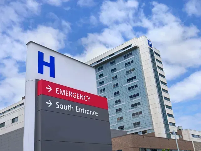 A hospital building with a sign pointing to the emergency room and south entrance.