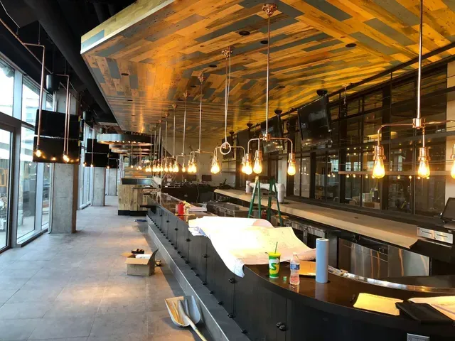 A long bar in a restaurant under construction with lots of lights hanging from the ceiling.