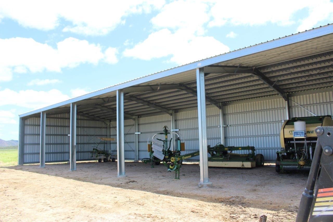 A row of tractors are parked under a shed.