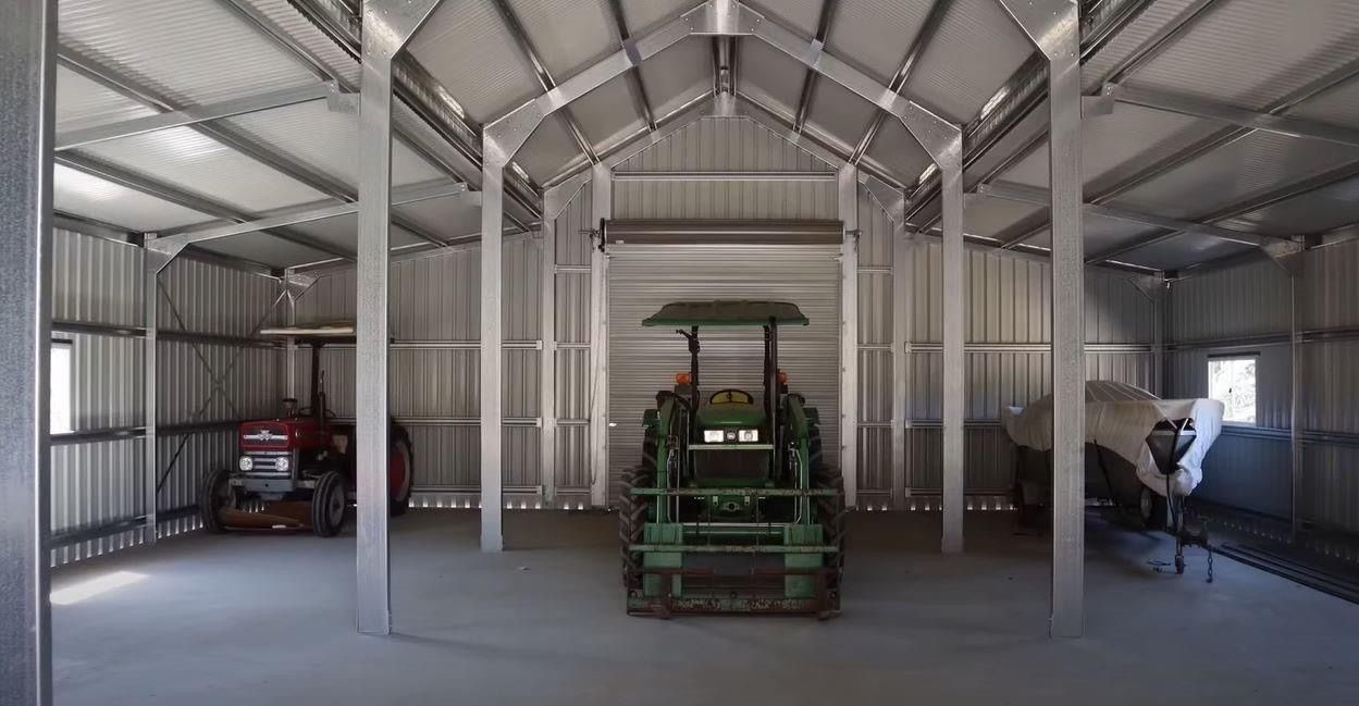 A green tractor is parked inside of a metal building.