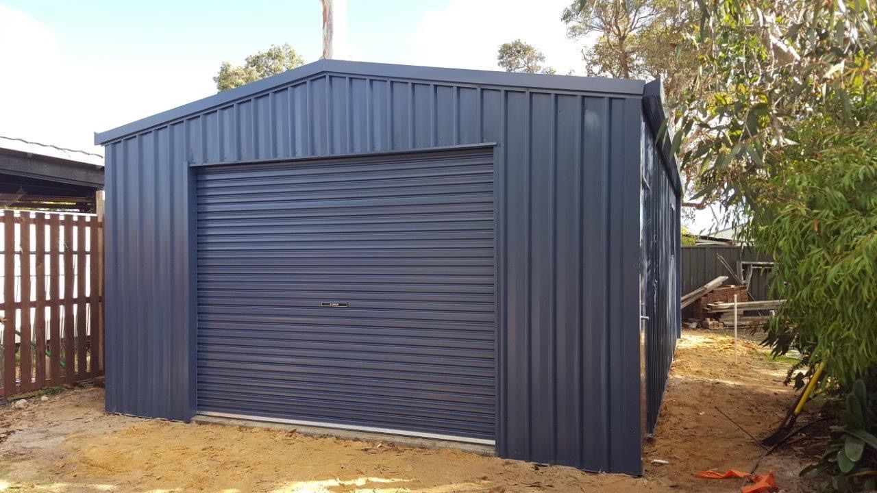 A blue garage with a roller door is sitting in the dirt next to a fence.