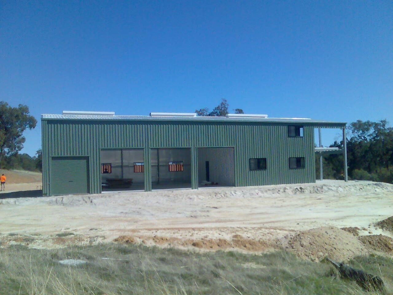 A large green building is sitting in the middle of a dirt field.