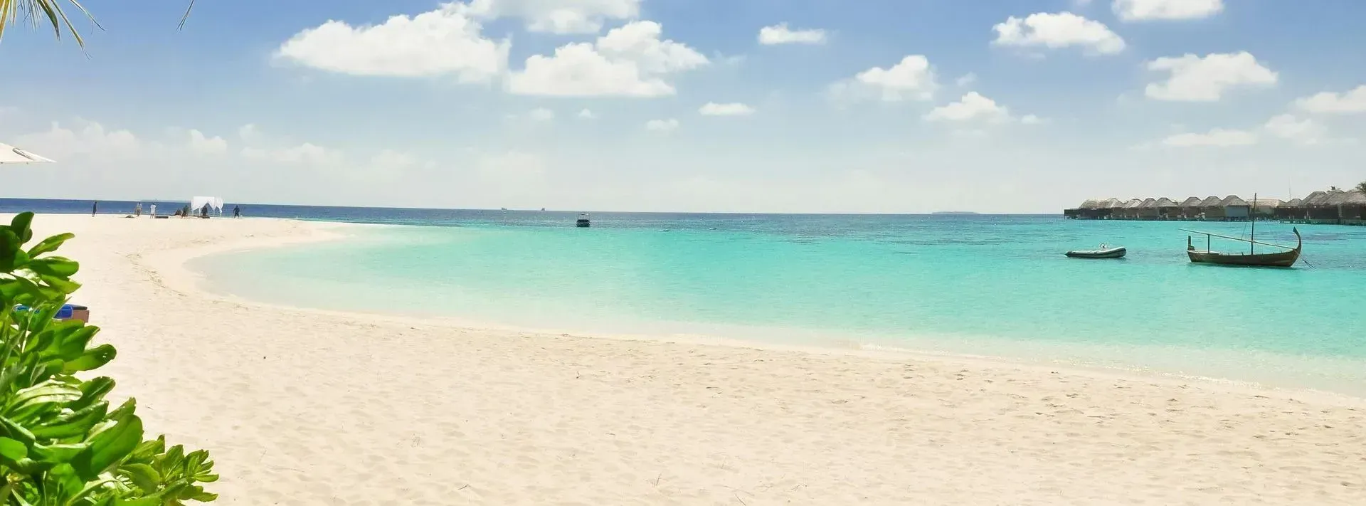 White sand beach with turquoise water under a blue sky with fluffy clouds. Boats dot the water.