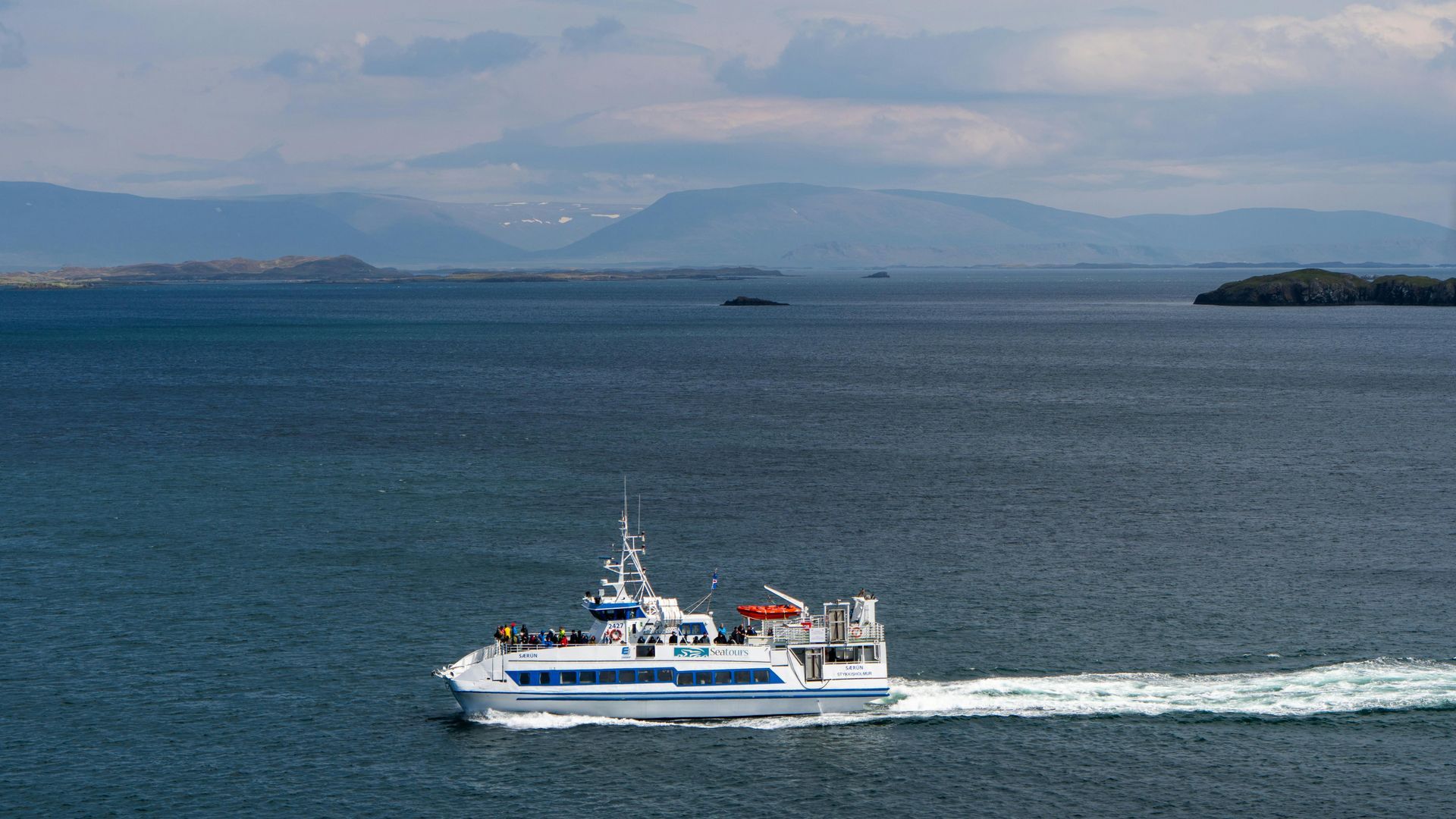 White ferry on blue water with mountains in the background.