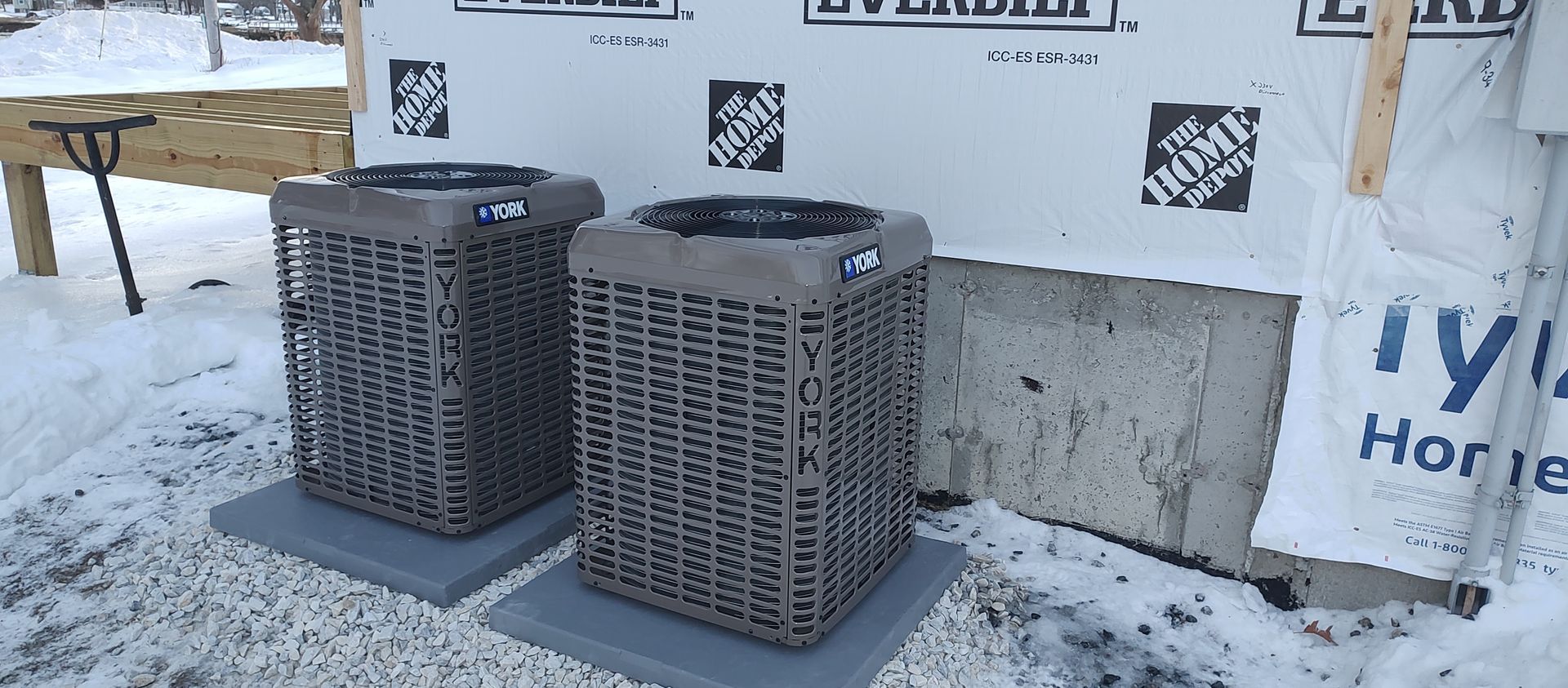 Two air conditioners are sitting in front of a home depot wall