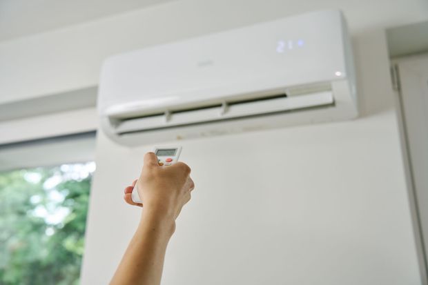 A person is using a remote control to turn on an air conditioner.