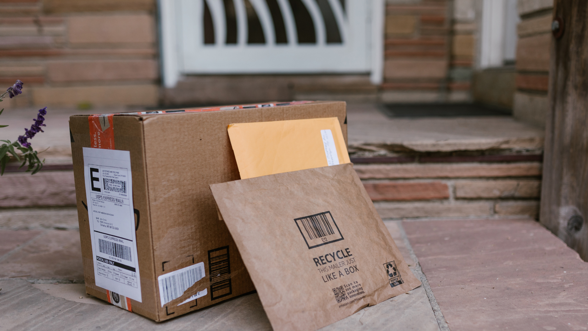 A cardboard box with an envelope in it is sitting on a porch next to a door.