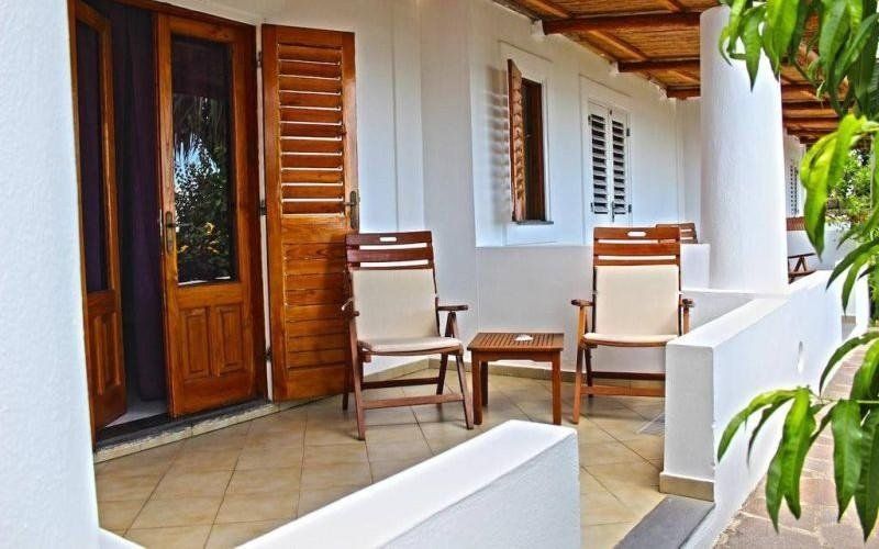 Veranda coperta con sedie in legno, tavolino e pareti in stucco bianco accanto a una porta in legno.