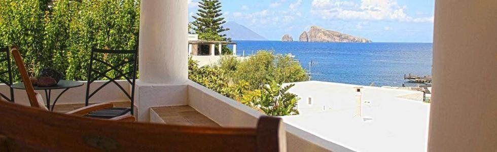 Patio ombreggiato con vista su un oceano di un blu intenso, con isole e edifici bianchi in lontananza.