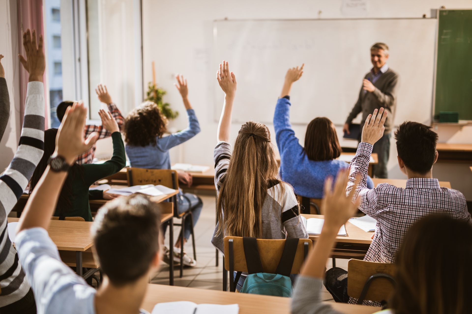 Un gruppo di studenti alza la mano in classe per rispondere a una domanda.