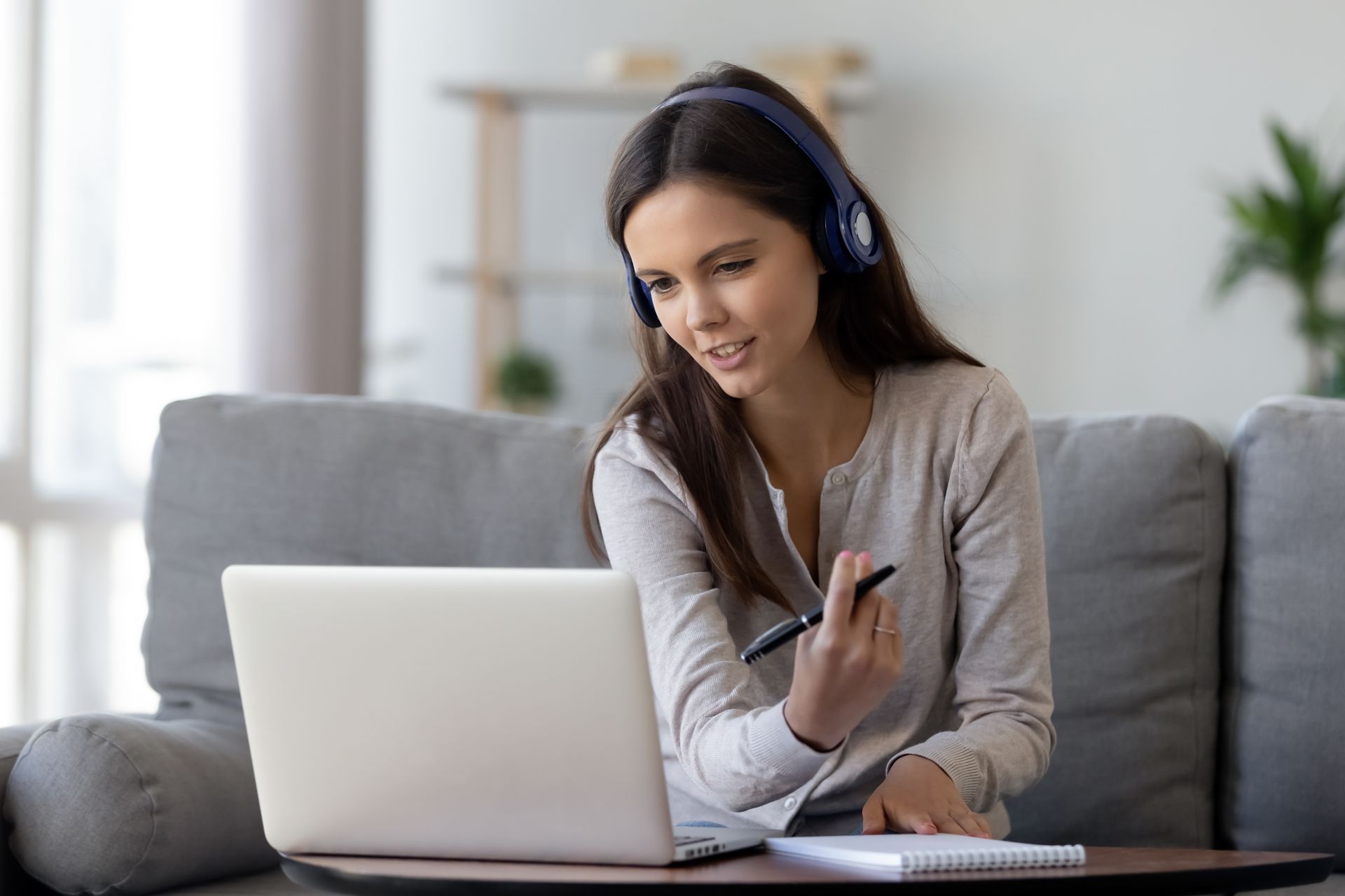 Una donna seduta su un divano sta usando un computer portatile e indossa delle cuffie.
