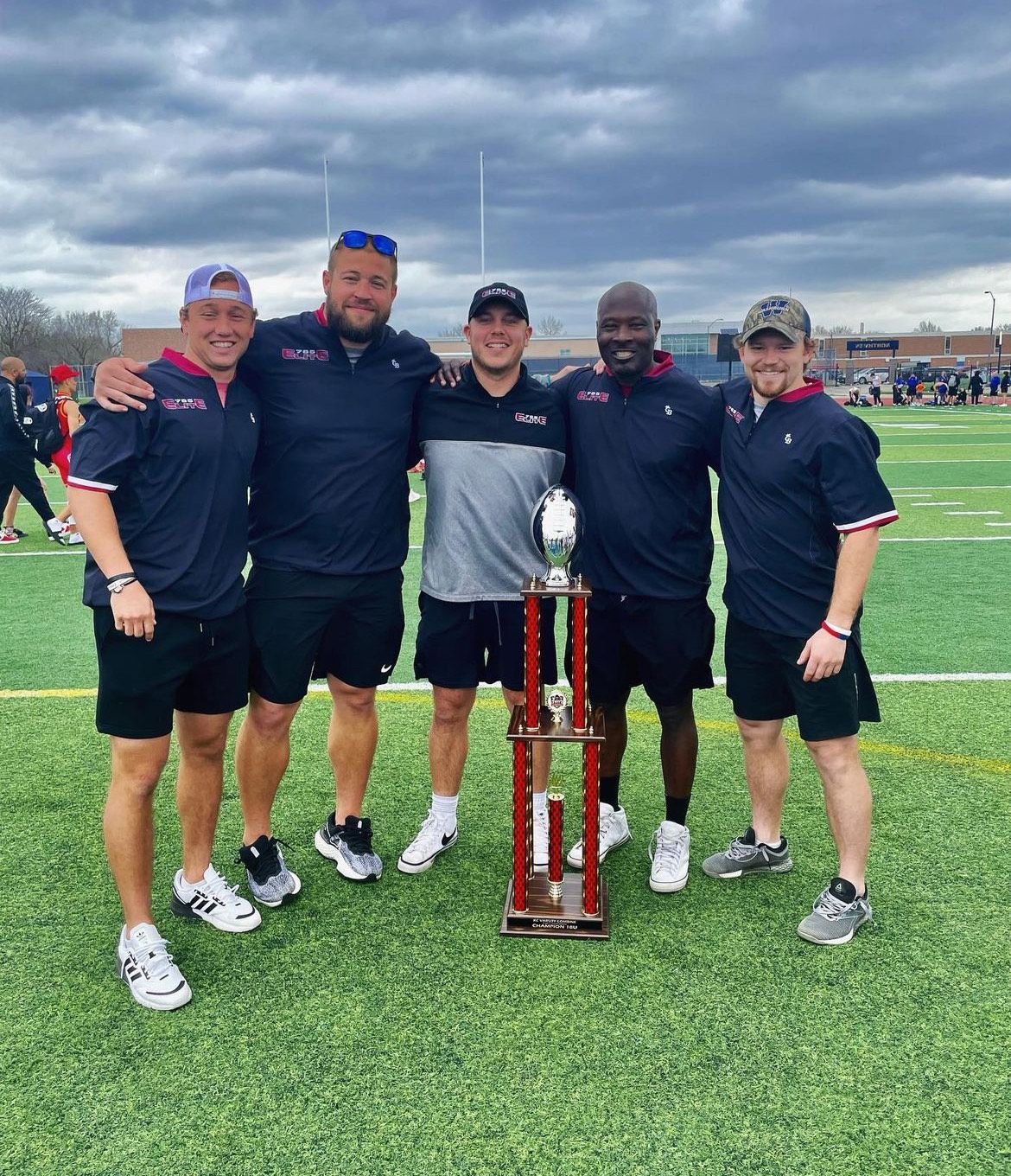 A group of men are posing for a picture on a football field with a trophy.