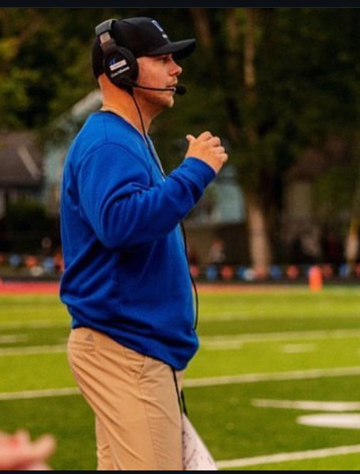 A man wearing headphones stands on a football field