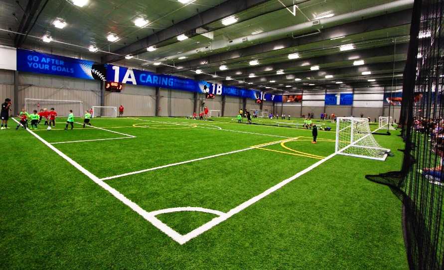 A group of children are playing soccer in an indoor stadium.