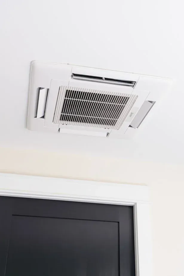 A white air conditioner is hanging from the ceiling next to a black door.