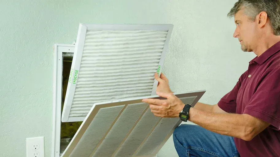 A man is cleaning an air vent with a filter.