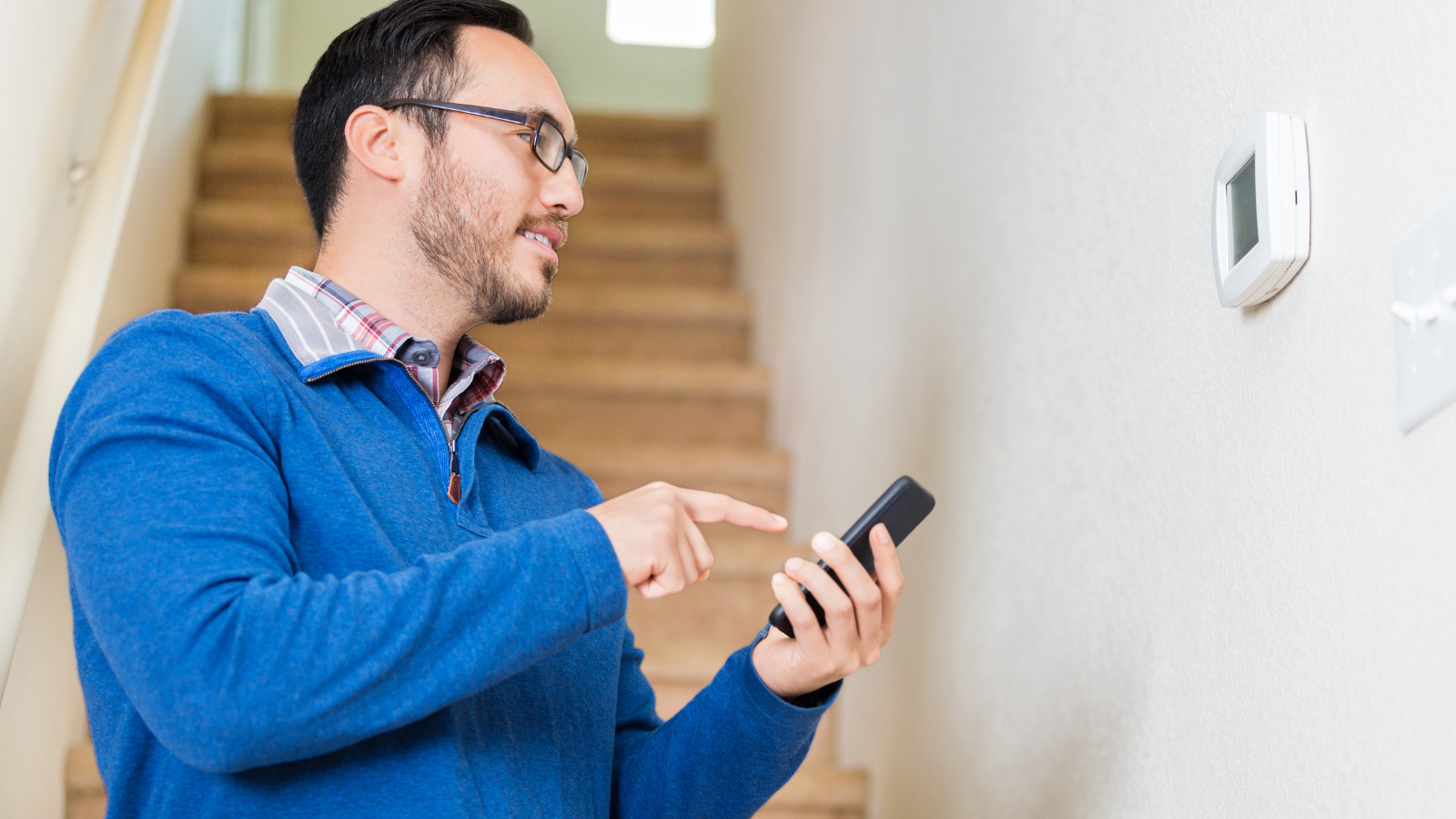 Man in blue sweater managing his smart thermostat with his phone